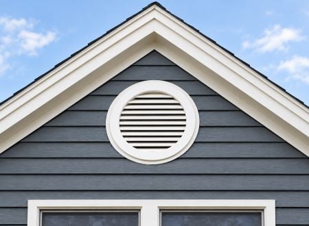 Charming brick garage with dual wooden doors, framed by elegant planters; featuring gable vents that enhance ventilation and architectural appeal against a clear blue sky.